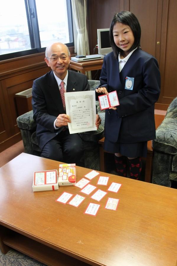 「新ひょうご風土記かるた」優秀賞を受賞した城北小学校5年生小林優希さんが右側に立って両手にかるたを持ち、左側に市長が表彰状を手に持っている記念写真